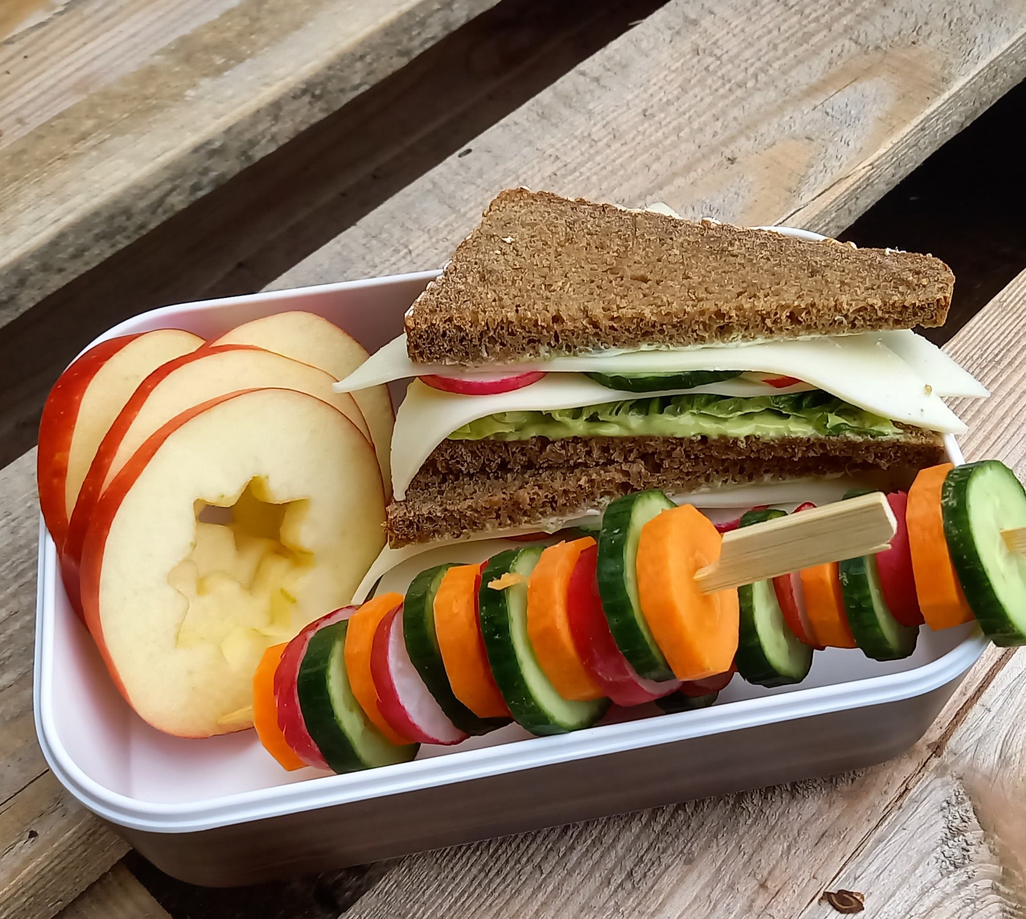 eine Lunchbox mit gesundem Essen: Vollkornsandwich, Äpfel, Gemüsespieße